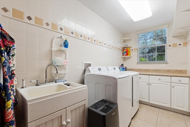 washroom with light tile patterned floors, a sink, tile walls, cabinet space, and washing machine and clothes dryer