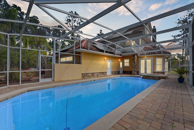 pool at dusk featuring a patio area, a pool with connected hot tub, glass enclosure, and french doors