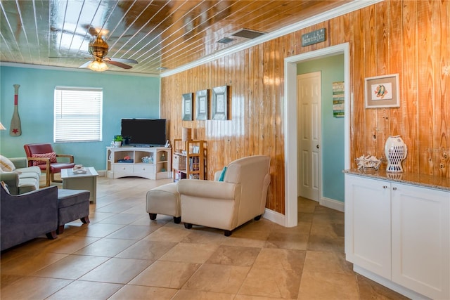 living room featuring wooden walls, baseboards, a ceiling fan, wooden ceiling, and crown molding