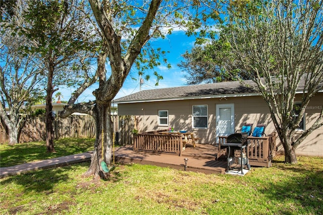 rear view of property featuring a deck, a lawn, and fence