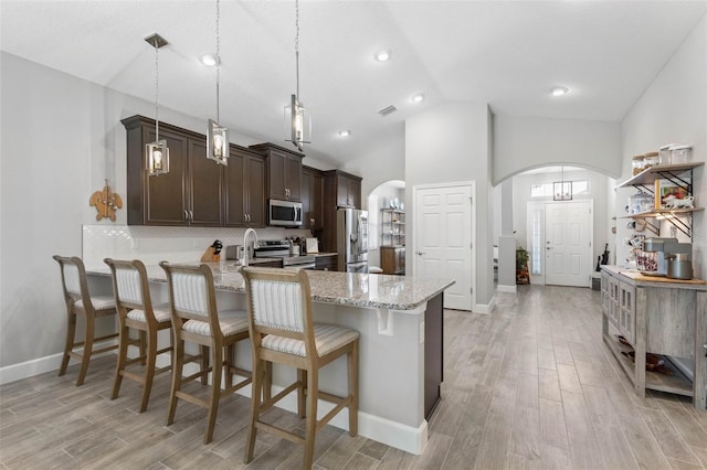 kitchen with stainless steel appliances, arched walkways, light wood finished floors, and dark brown cabinets