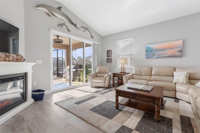 living room with vaulted ceiling, wood finished floors, a glass covered fireplace, and baseboards