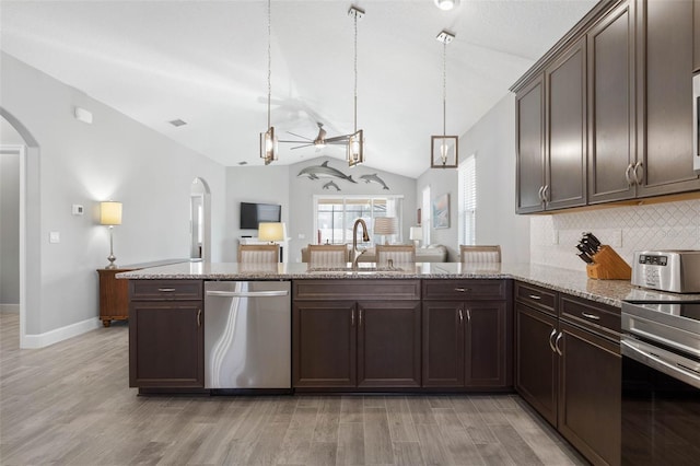 kitchen featuring dark brown cabinetry, appliances with stainless steel finishes, arched walkways, and a sink