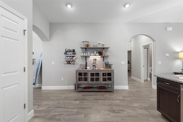 bar featuring arched walkways, light wood-type flooring, and baseboards