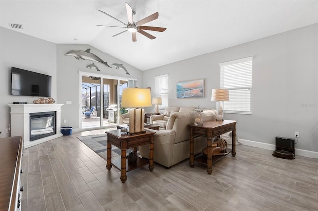 living area with visible vents, a glass covered fireplace, vaulted ceiling, ceiling fan, and light wood-type flooring