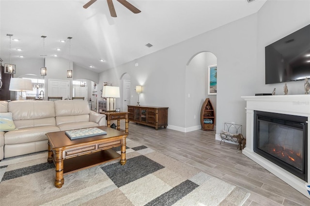 living room featuring arched walkways, lofted ceiling, visible vents, wood tiled floor, and a glass covered fireplace