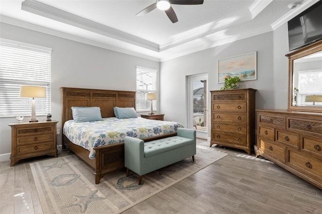 bedroom with ornamental molding, a tray ceiling, and light wood-type flooring