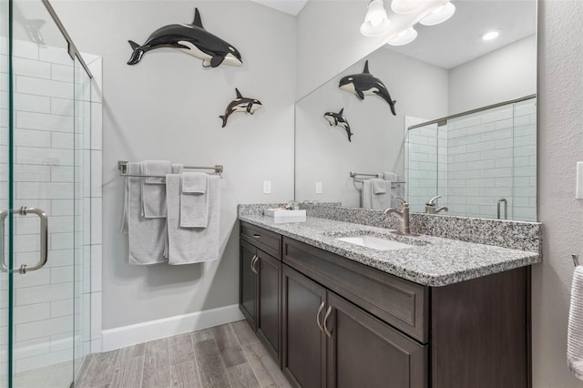 full bath with double vanity, a stall shower, a sink, and wood finished floors