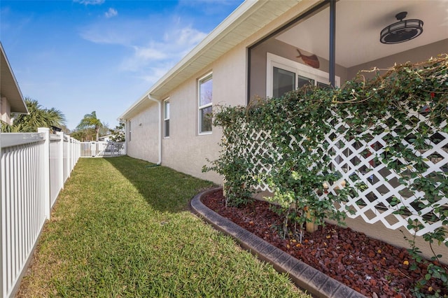 view of property exterior featuring a fenced backyard, ceiling fan, a lawn, and stucco siding