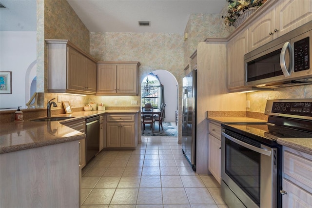 kitchen featuring arched walkways, visible vents, appliances with stainless steel finishes, a sink, and wallpapered walls