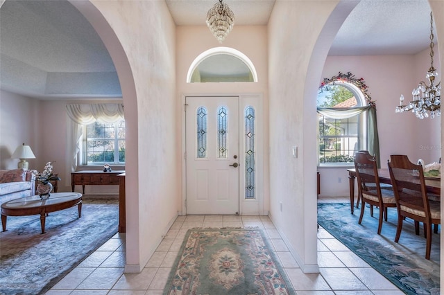 foyer with a chandelier, arched walkways, a textured ceiling, and light tile patterned floors