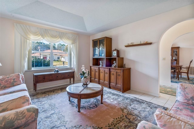 living area featuring light tile patterned floors, baseboards, arched walkways, and a raised ceiling