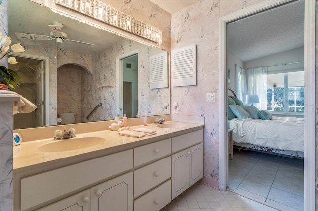 ensuite bathroom featuring toilet, wallpapered walls, connected bathroom, and a sink