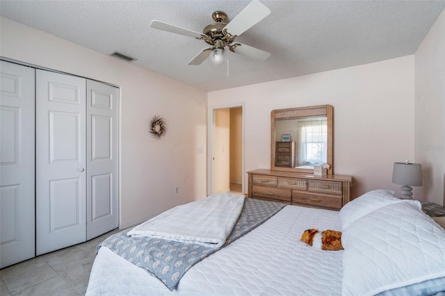 bedroom featuring light tile patterned floors, visible vents, ceiling fan, a textured ceiling, and a closet