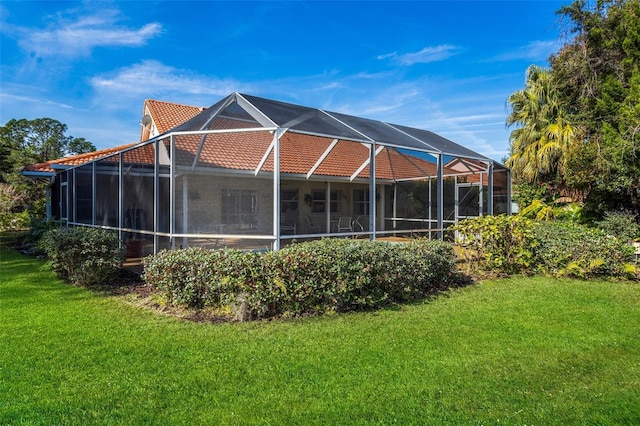 rear view of property featuring glass enclosure, a tile roof, and a lawn