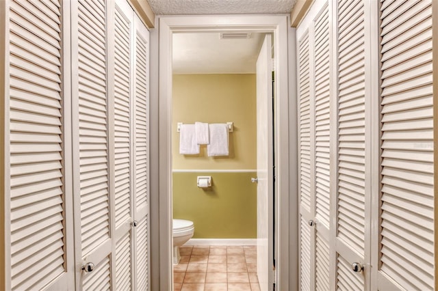 bathroom featuring a textured ceiling, tile patterned flooring, toilet, visible vents, and a closet