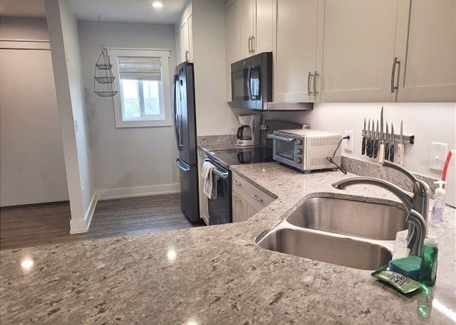 kitchen featuring black microwave, a sink, electric stove, freestanding refrigerator, and light stone countertops