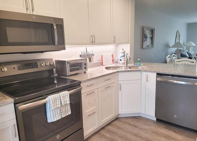 kitchen featuring stainless steel appliances, light wood-style floors, white cabinetry, a sink, and light stone countertops