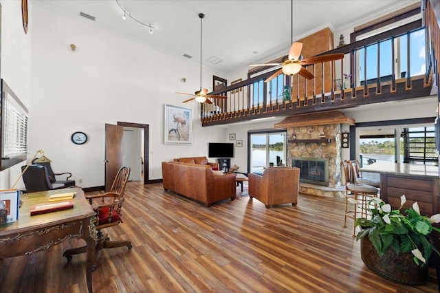 living area featuring visible vents, ornamental molding, a ceiling fan, a stone fireplace, and wood finished floors