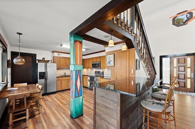 kitchen featuring appliances with stainless steel finishes, backsplash, a peninsula, light wood-style floors, and a sink