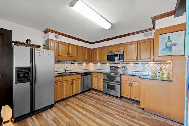 kitchen featuring stainless steel appliances, visible vents, light wood-style flooring, decorative backsplash, and a sink