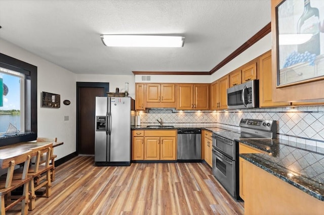 kitchen with stainless steel appliances, a sink, light wood-style flooring, and decorative backsplash