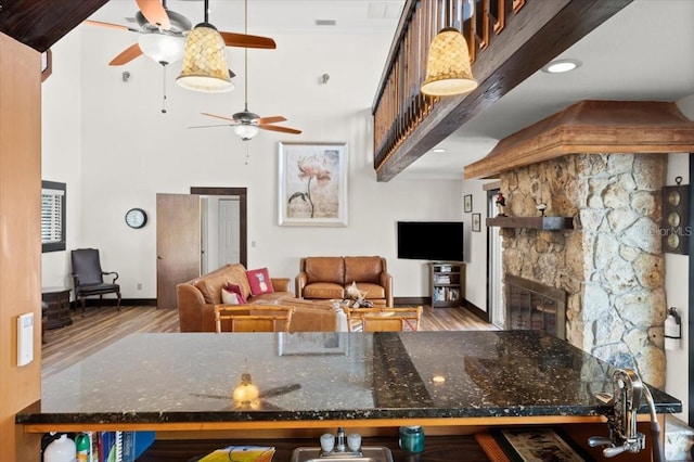 kitchen featuring a towering ceiling, dark stone counters, wood finished floors, and a stone fireplace