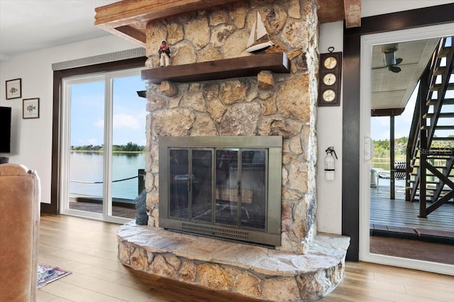 living room with stairs, a stone fireplace, a water view, and wood finished floors