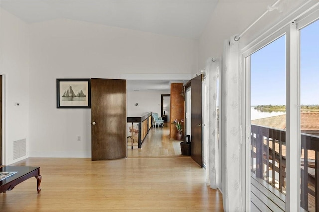 hall with lofted ceiling, a water view, visible vents, baseboards, and light wood-style floors