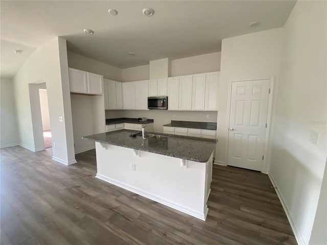 kitchen with stainless steel microwave, a sink, white cabinets, dark wood-style floors, and an island with sink