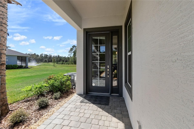 property entrance featuring a water view, a lawn, and stucco siding