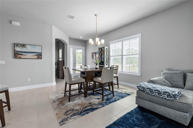 dining area featuring arched walkways, light tile patterned flooring, a notable chandelier, visible vents, and baseboards