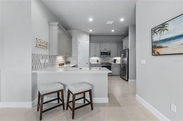 kitchen with a peninsula, a sink, gray cabinets, stainless steel appliances, and backsplash