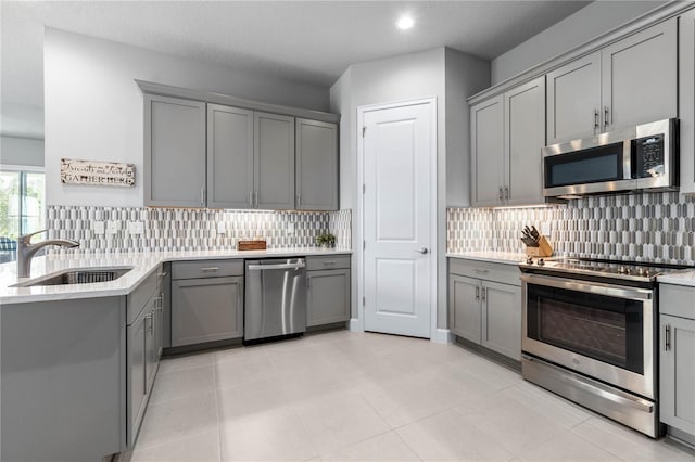 kitchen featuring stainless steel appliances, light countertops, a sink, and gray cabinetry