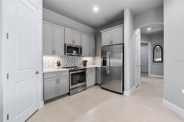 kitchen with arched walkways, decorative backsplash, appliances with stainless steel finishes, light countertops, and gray cabinetry