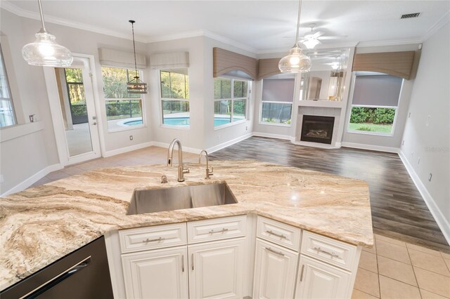 kitchen featuring a sink, light stone counters, a fireplace, crown molding, and dishwasher