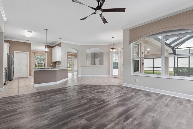 unfurnished living room featuring crown molding, a ceiling fan, light wood-type flooring, and a wealth of natural light