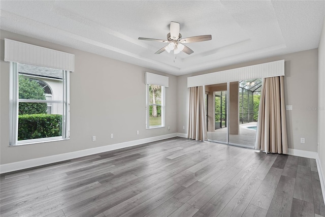 empty room featuring a tray ceiling, baseboards, and wood finished floors