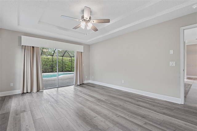 empty room with a ceiling fan, a raised ceiling, wood finished floors, and baseboards