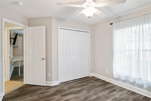 unfurnished bedroom featuring a closet, a textured ceiling, baseboards, and dark wood-style flooring