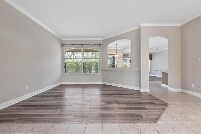 empty room with arched walkways, crown molding, baseboards, and wood finished floors