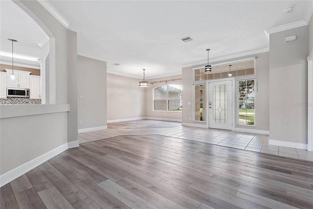 unfurnished living room featuring visible vents, baseboards, light wood-style floors, and ornamental molding