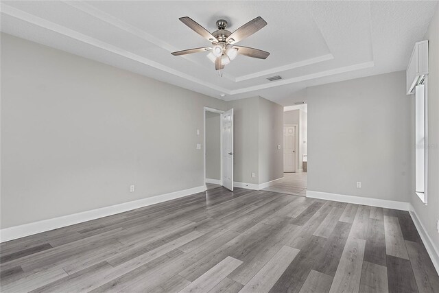 empty room featuring a tray ceiling, wood finished floors, visible vents, and baseboards