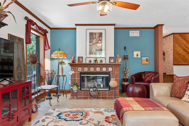 living room featuring a ceiling fan, visible vents, baseboards, a tile fireplace, and ornamental molding