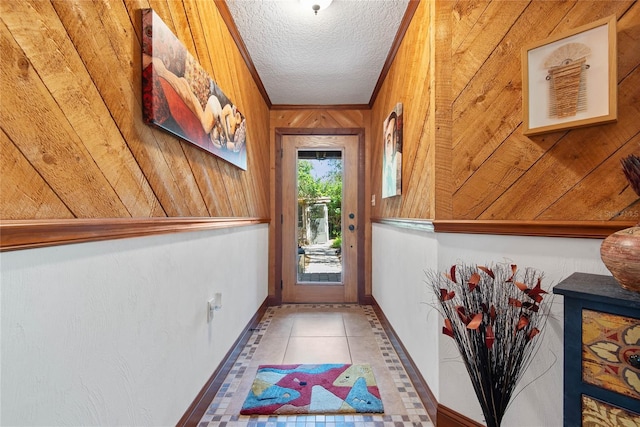 entryway featuring ornamental molding, a textured ceiling, wooden walls, tile patterned flooring, and baseboards