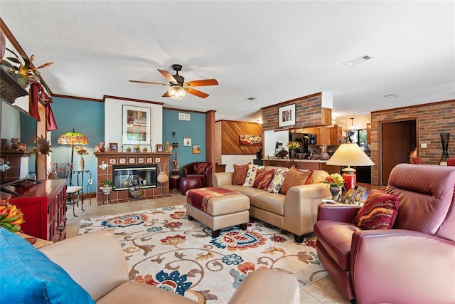 tiled living room featuring a ceiling fan, visible vents, a tile fireplace, a textured ceiling, and crown molding