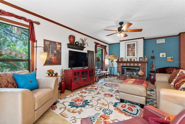 living room with a tiled fireplace, crown molding, visible vents, and ceiling fan