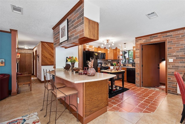 kitchen featuring black appliances, a kitchen breakfast bar, light countertops, and visible vents
