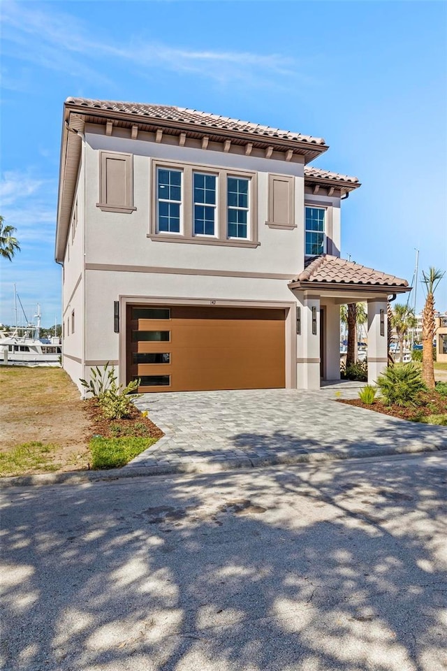 view of front of property with a tiled roof, decorative driveway, an attached garage, and stucco siding