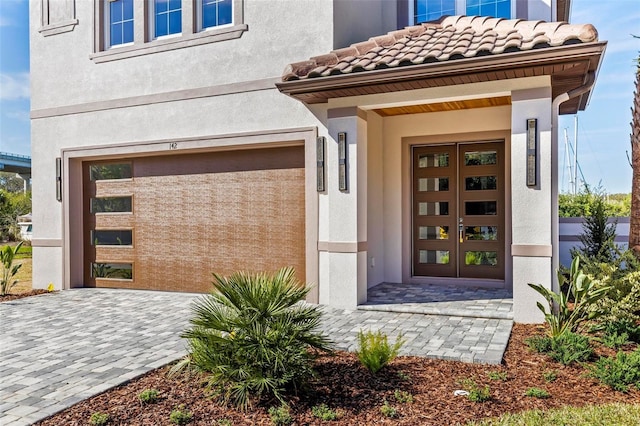 view of exterior entry featuring a tiled roof, french doors, decorative driveway, and stucco siding